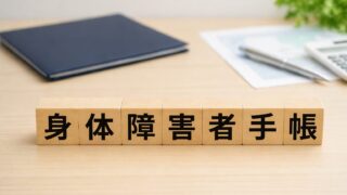 身体障害者手帳と書かれた木製ブロックとノートと電卓
