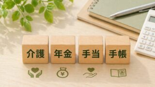 介護・年金・手当・手帳と書かれた木製ブロックとノートと電卓と観葉植物